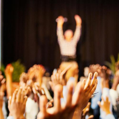 Hands of a crowd raised at a speaker on the stage