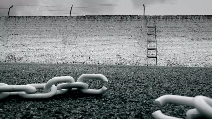 White broke chain in front of an enclosure wall. A ladder stands again the wall. 