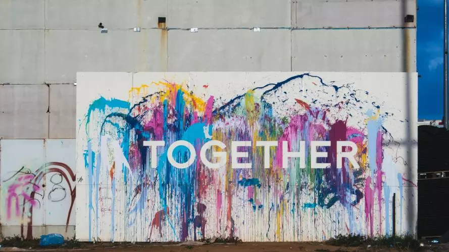 Graffiti on concrete wall. The word 'together' is written in white bold letters agains a background of colourful splash 