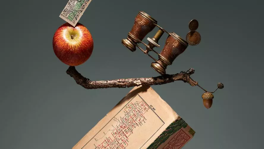 Absurd picture where a series of objects, including an apple, a pencil, a book, a pair of binoculars etc are impossibly balanced on top each other to prompt the viewer's interest.