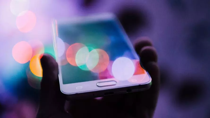 hand holding smartphone with colourful light reflections all over