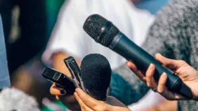 Hands holding microphones and recording devices in front of an unseen speaker