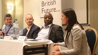Photograph of discussing in one of British Future's events, in front of the organisation's logo. The panelists are of different genders and ethnic groups
