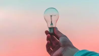 Photo of a hand holding a lightbulb against the sunset