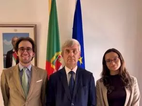 The student with two colleagues of hers in front of the Portuguese and European flags