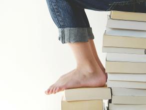 Picture of the lower body of a young person sitting on a stack of books while reading