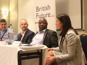 Photograph of discussing in one of British Future's events, in front of the organisation's logo. The panelists are of different genders and ethnic groups