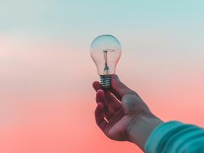 Photo of a hand holding a lightbulb against the sunset