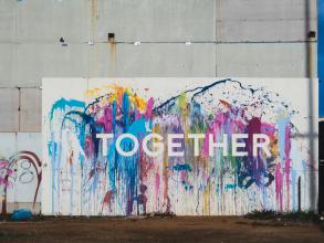 Graffiti on concrete wall. The word 'together' is written in white bold letters agains a background of colourful splash 
