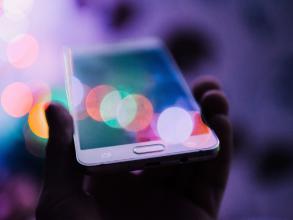 hand holding smartphone with colourful light reflections all over