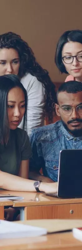 A group of students gather around a laptop in a lecture theatre