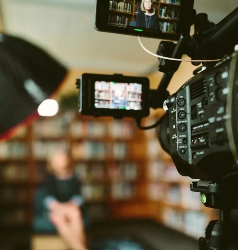 Person sitting in front of a bookshelf being filmed